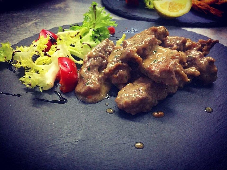 Beef stew on a dark plate with salad greens and tomato garnish