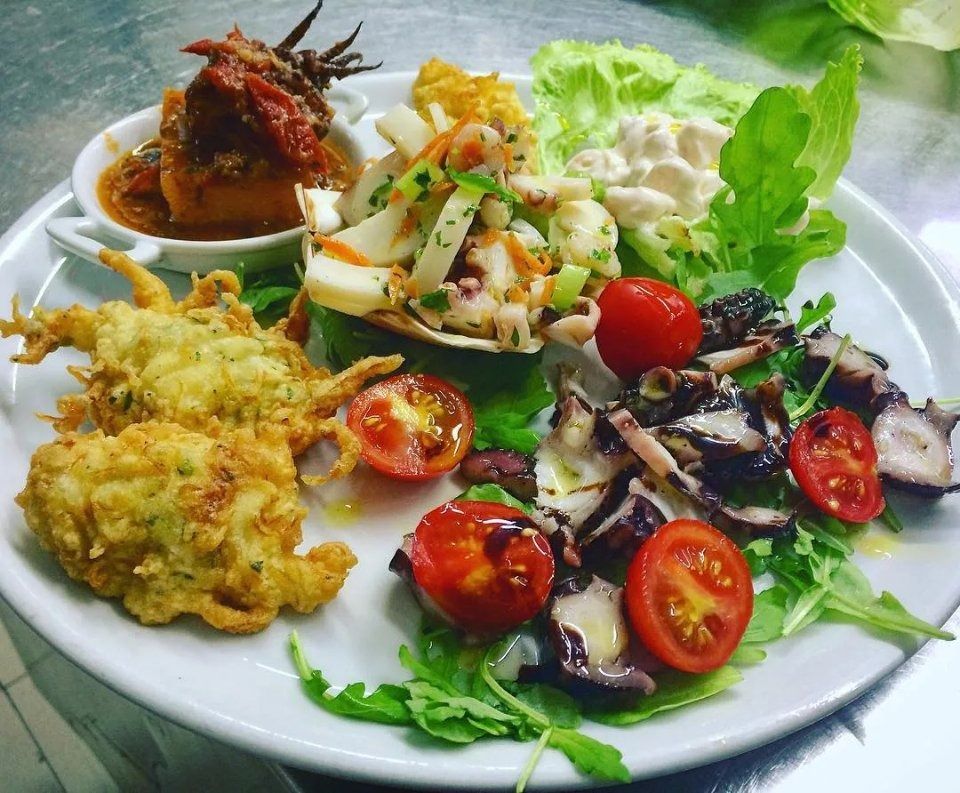 Assorted colorful appetizers and salads arranged on a white plate with greens and cherry tomatoes