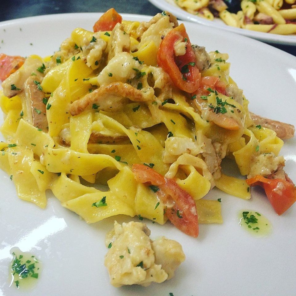 Plate of yellow pasta with creamy sauce, herbs, tomatoes, and seafood pieces