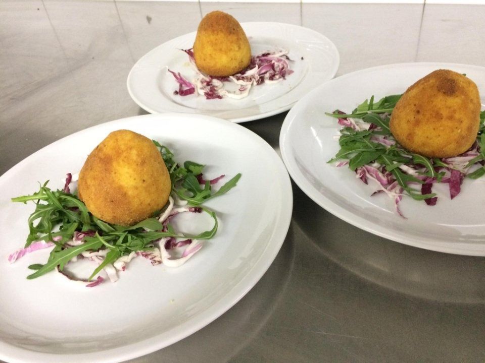 Three plated fried balls on a bed of greens and purple onions on a stainless steel counter