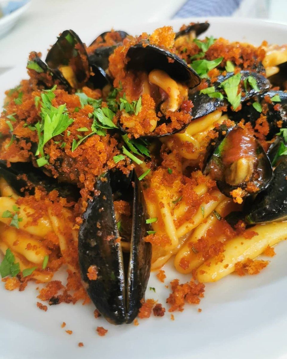 Mussels and fries topped with tomato sauce, herbs, and crispy breadcrumbs on a white plate