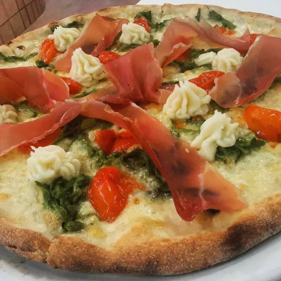 Pizza condita con prosciutto, pomodori, pesto al basilico e formaggio cremoso su un piatto