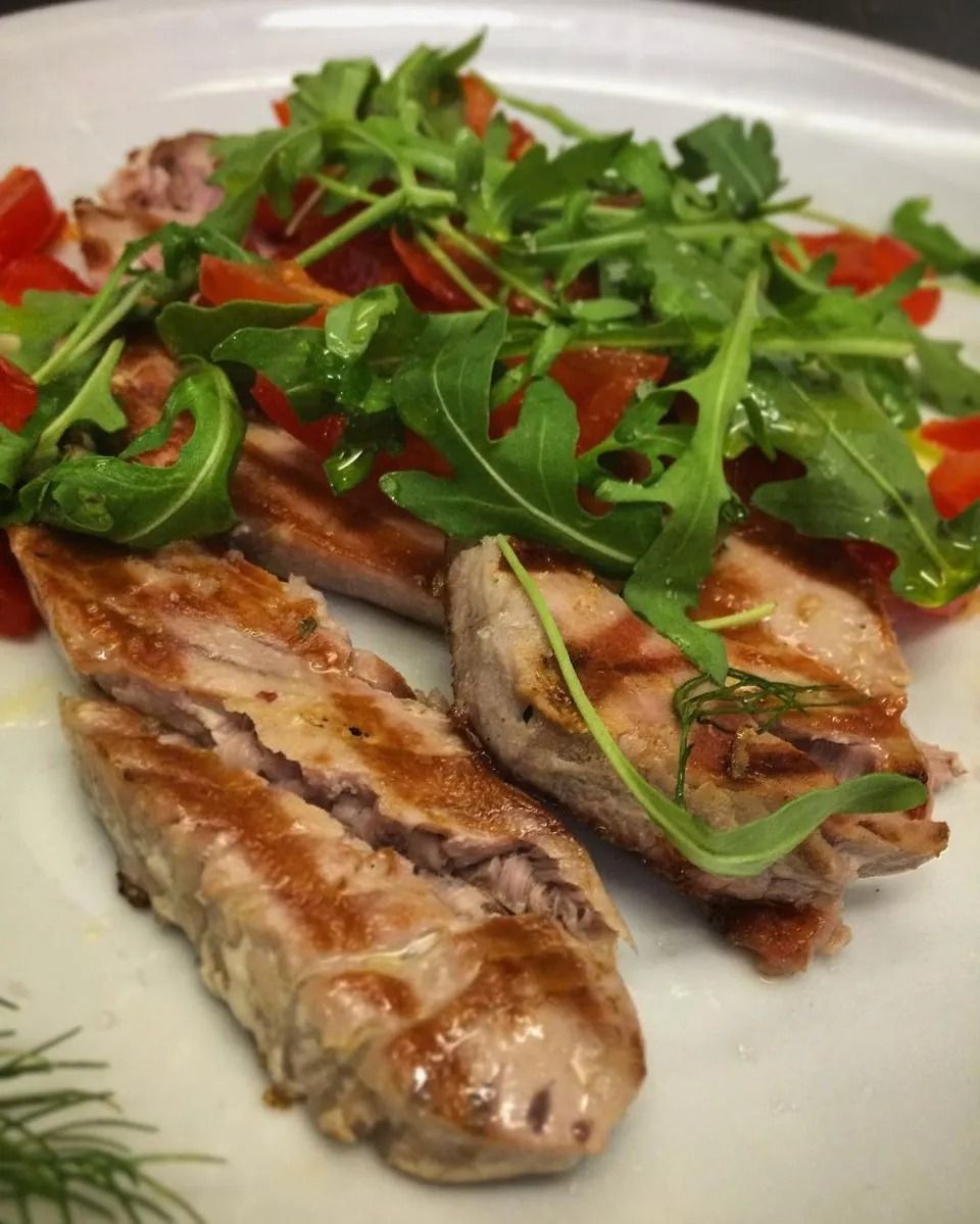 Grilled fish fillets topped with arugula and cherry tomatoes on a white plate