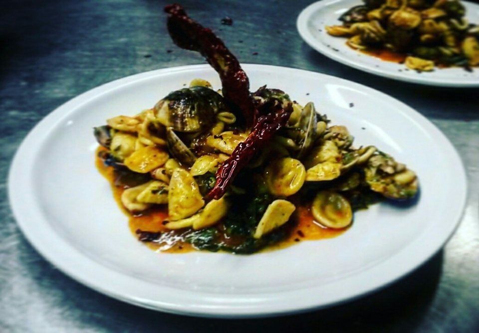 Plated pasta with clams and dark sauce, topped with a red chili pepper, on a table
