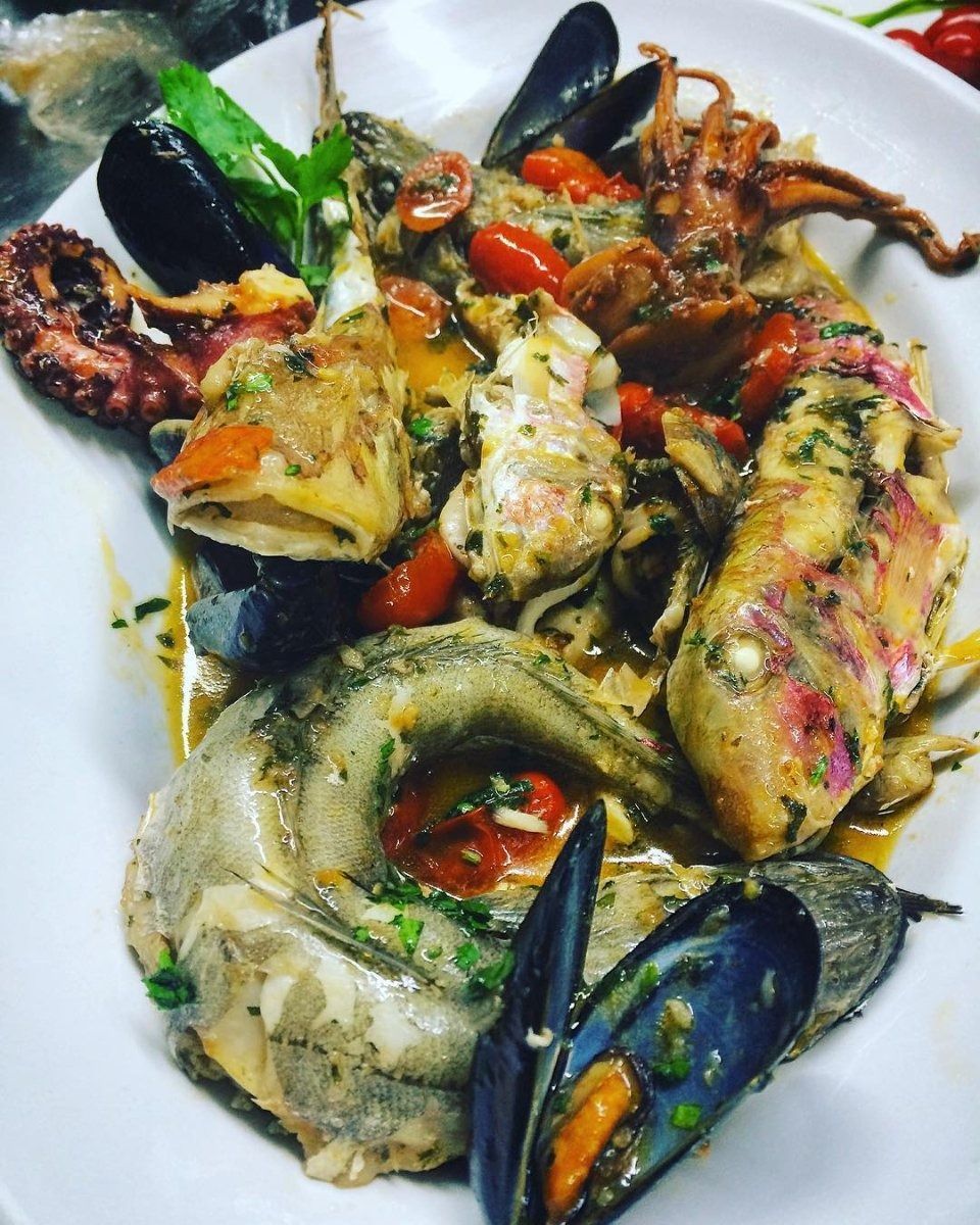 Seafood platter with mussels, lobster, and grilled fish on a white plate, topped with herbs and sauce