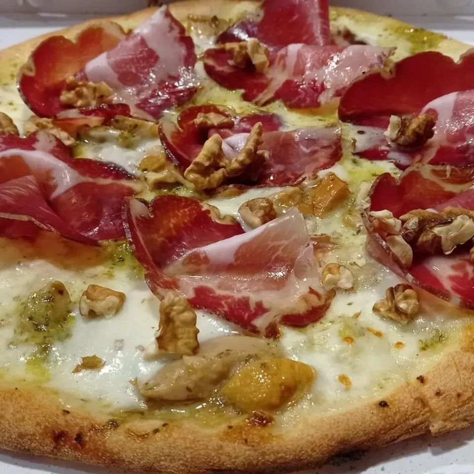 Primo piano di una pizza condita con prosciutto crudo, noci e formaggio fuso.