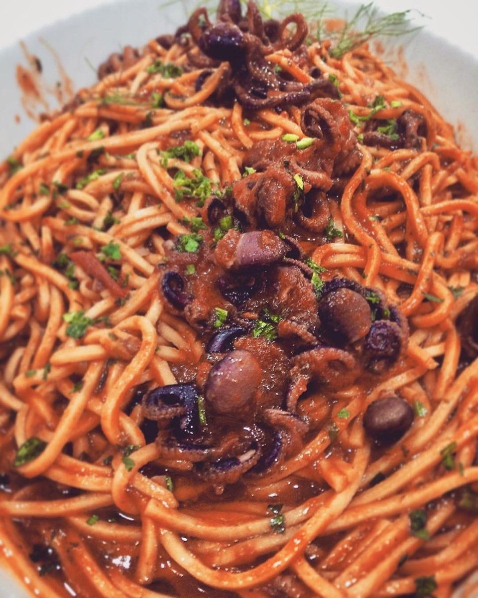 Spaghetti in red sauce topped with sliced mushrooms and herbs on a white plate