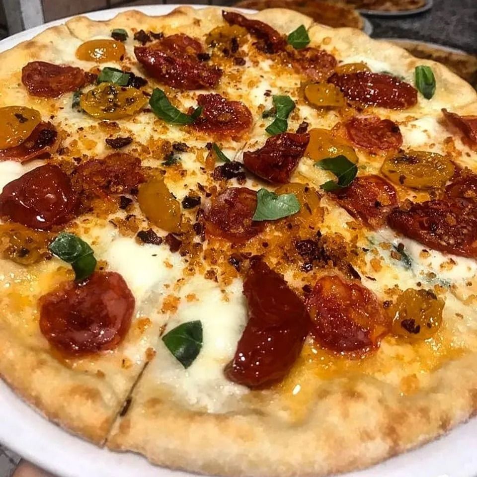 Pizza con salame piccante e pomodorini, formaggio fuso e basilico su tagliere di legno.