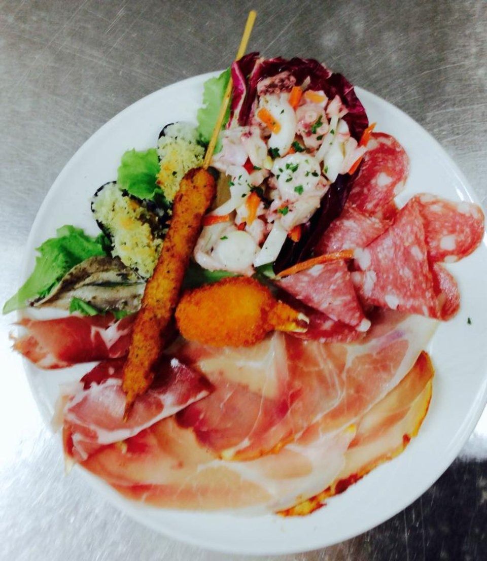 Seafood platter with shrimp, sliced salami, prosciutto, greens, and breadstick on a white plate