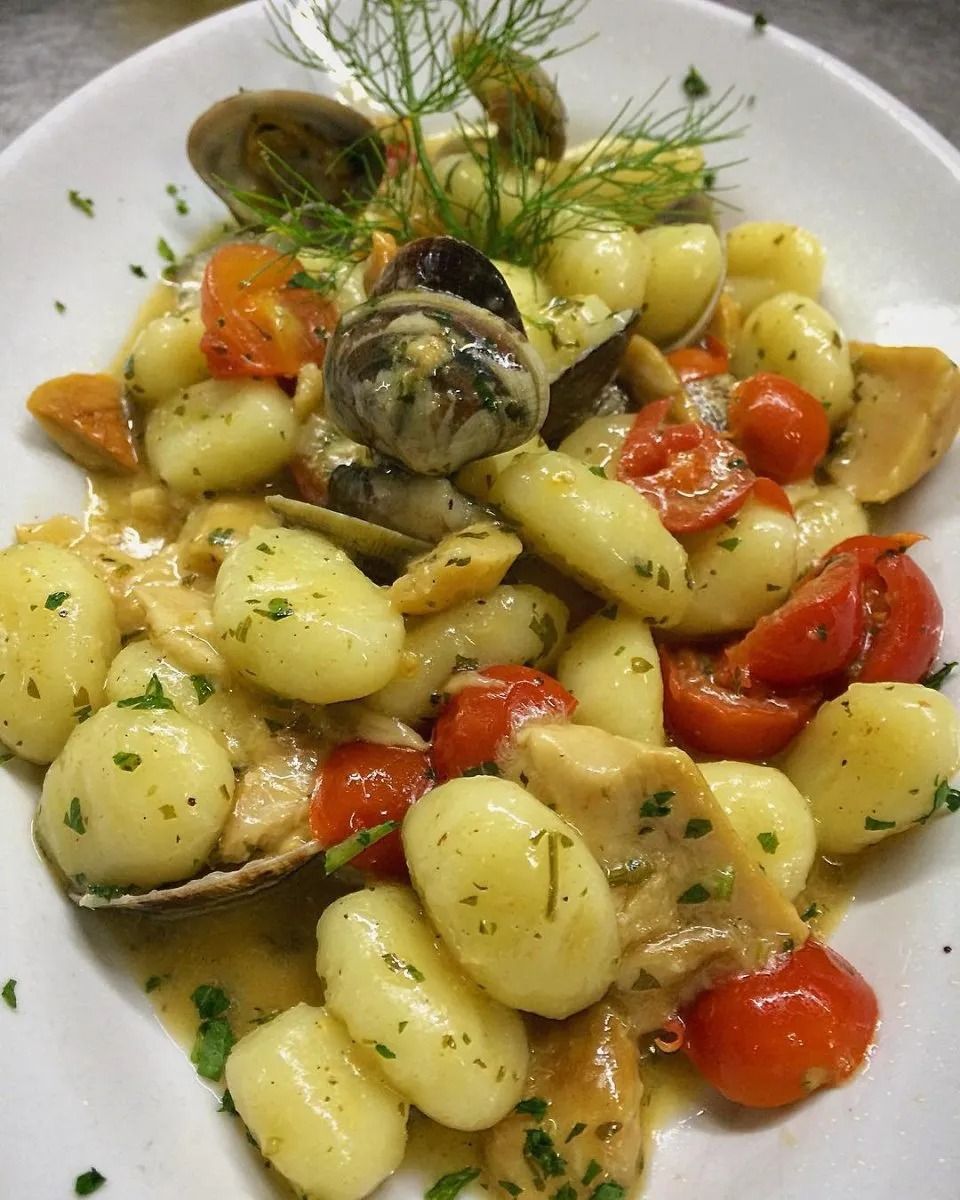 Gnocchi with tomatoes, herbs, and mushrooms on a white plate