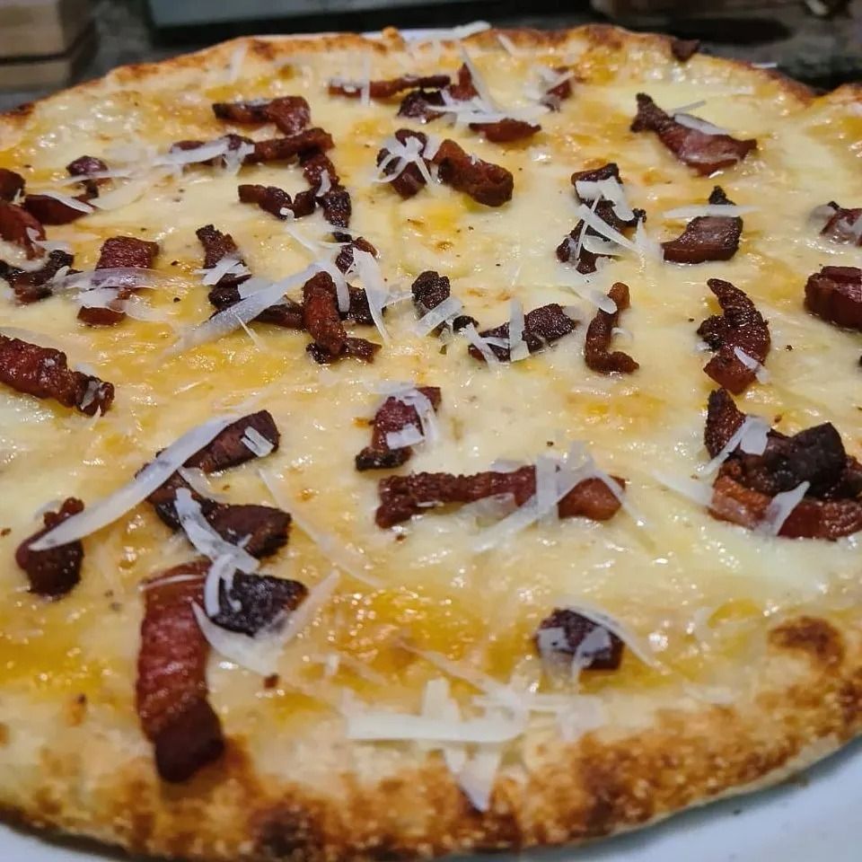 Primo piano di una pizza ricca di formaggio, guarnita con strisce scure simili a pancetta e formaggio grattugiato.