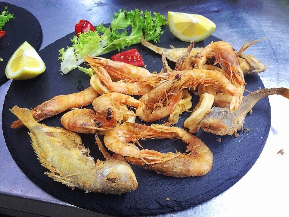 Plated fried shrimp and fish with lemon wedges and herbs on a black plate