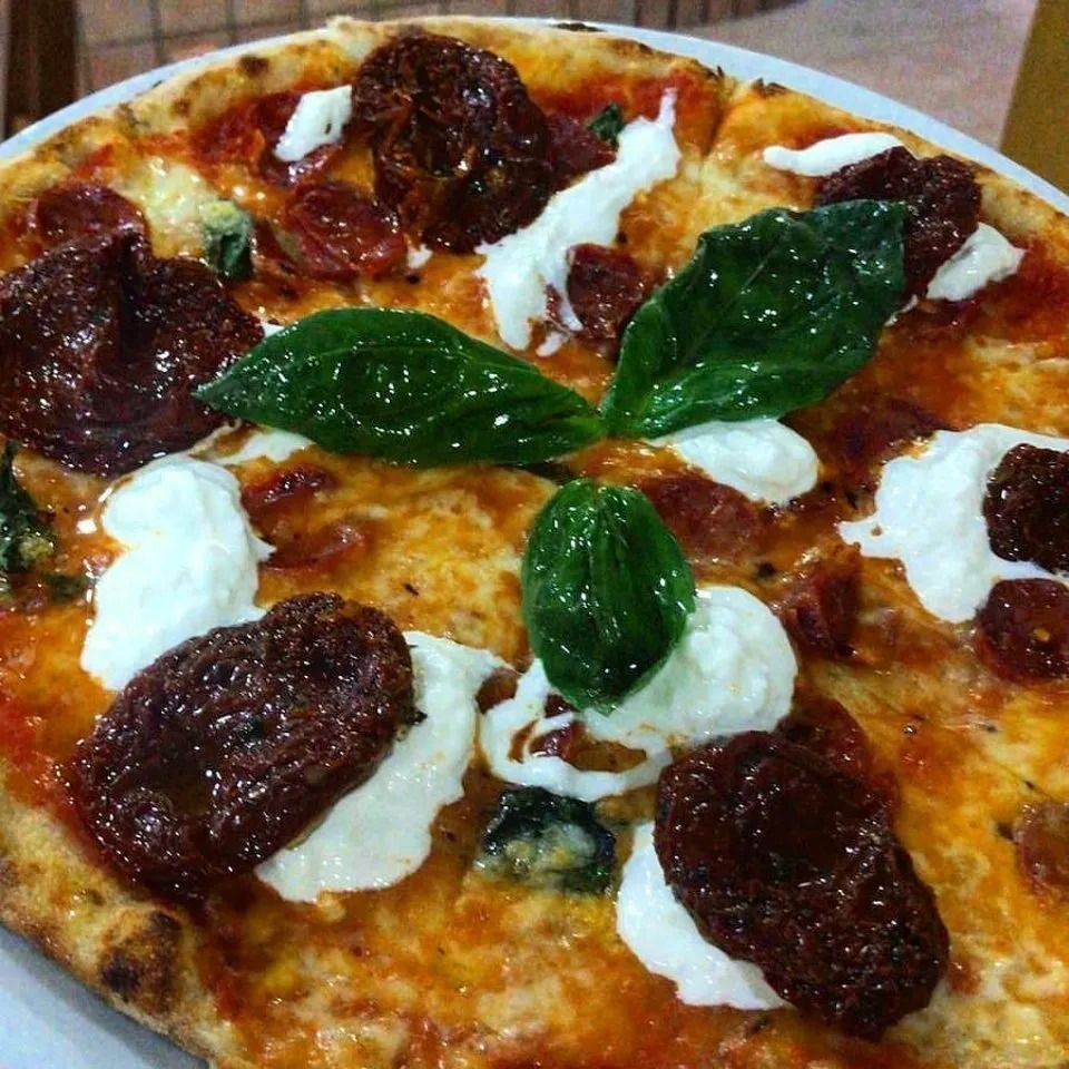 Primo piano di una pizza condita con foglie di basilico, mozzarella e pomodori secchi.
