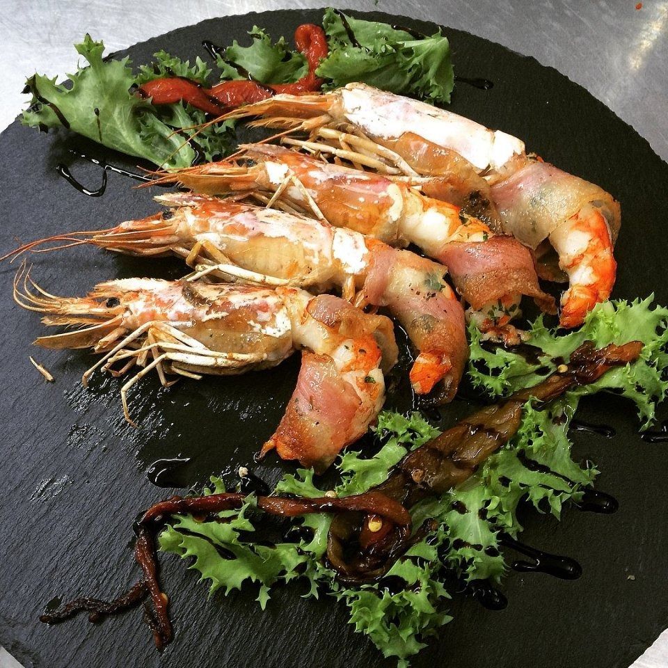 Grilled prawns on a black plate with greens and sauce drizzle
