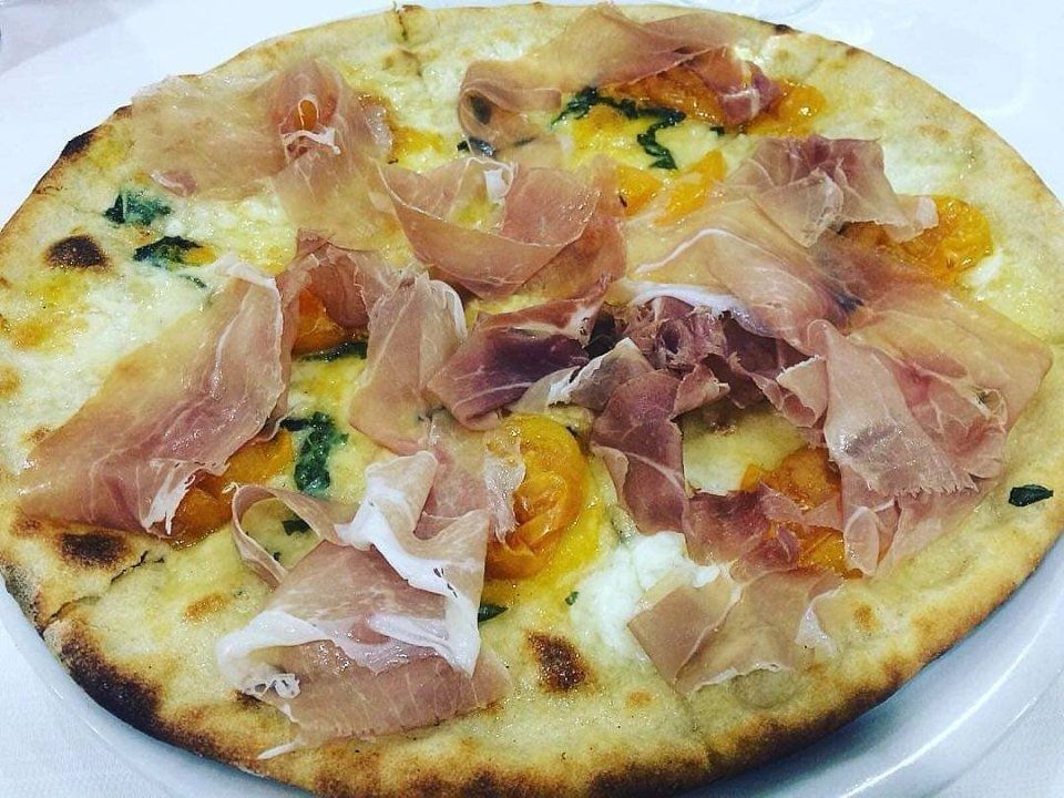 Pizza con prosciutto e formaggio fuso su un piatto bianco