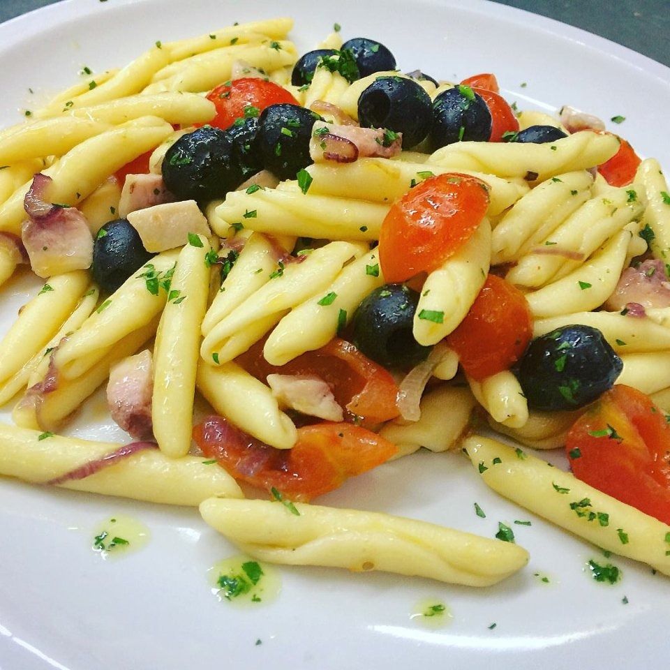 Pasta salad with penne, cherry tomatoes, black olives, and herbs on a white plate