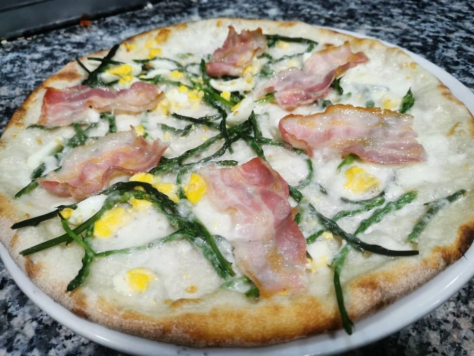 Pizza bianca condita con prosciutto rosa, erbe aromatiche verdi e ciuffi gialli su un piatto