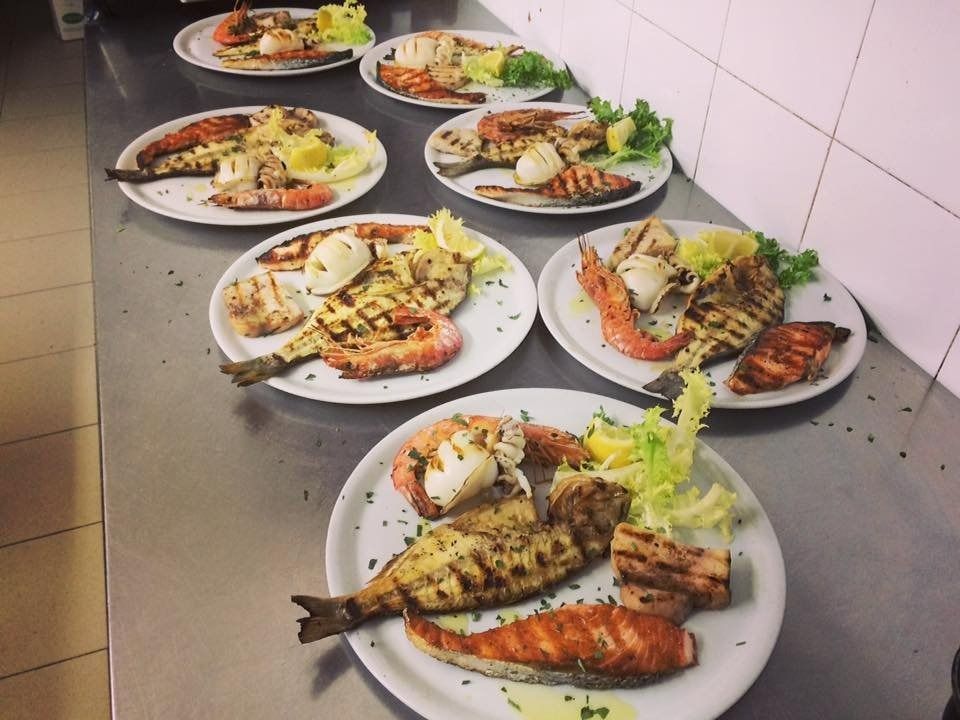 Plates of assorted grilled fish and garnishes arranged on a kitchen counter.