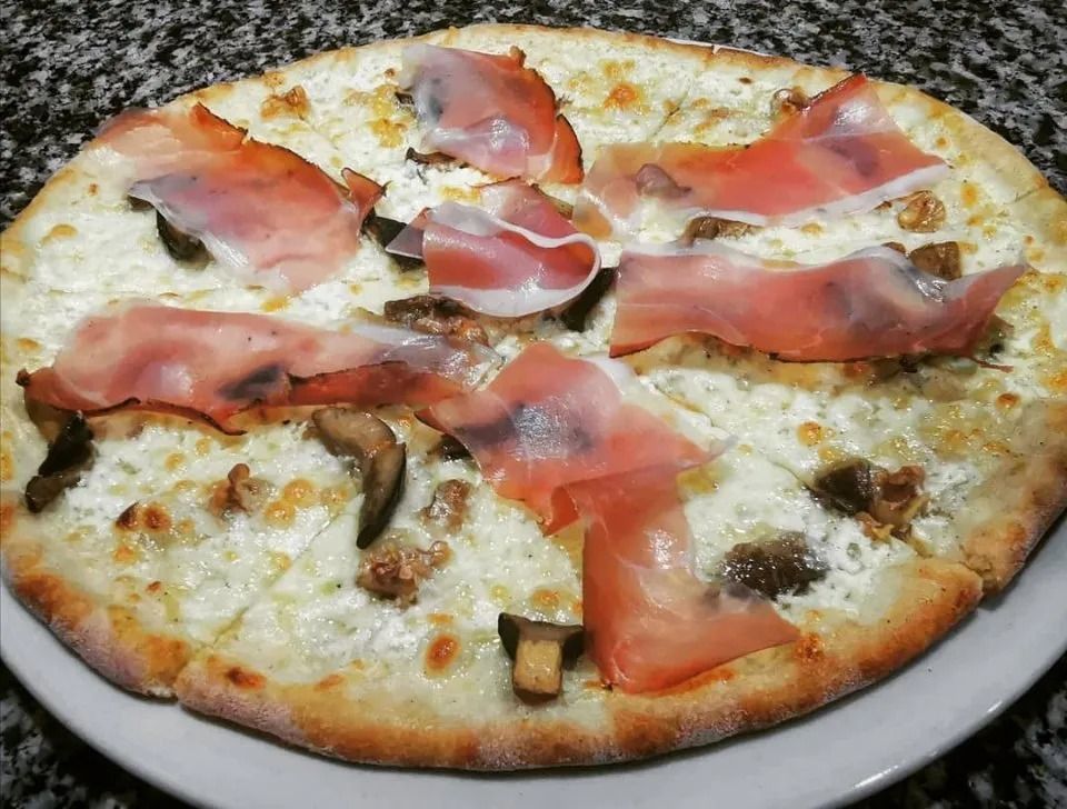 Pizza a crosta sottile su un piatto bianco, condita con formaggio fuso, funghi e fette di prosciutto.