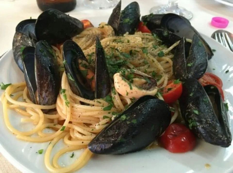 Spaghetti with mussels, shrimp, and cherry tomatoes on a white plate