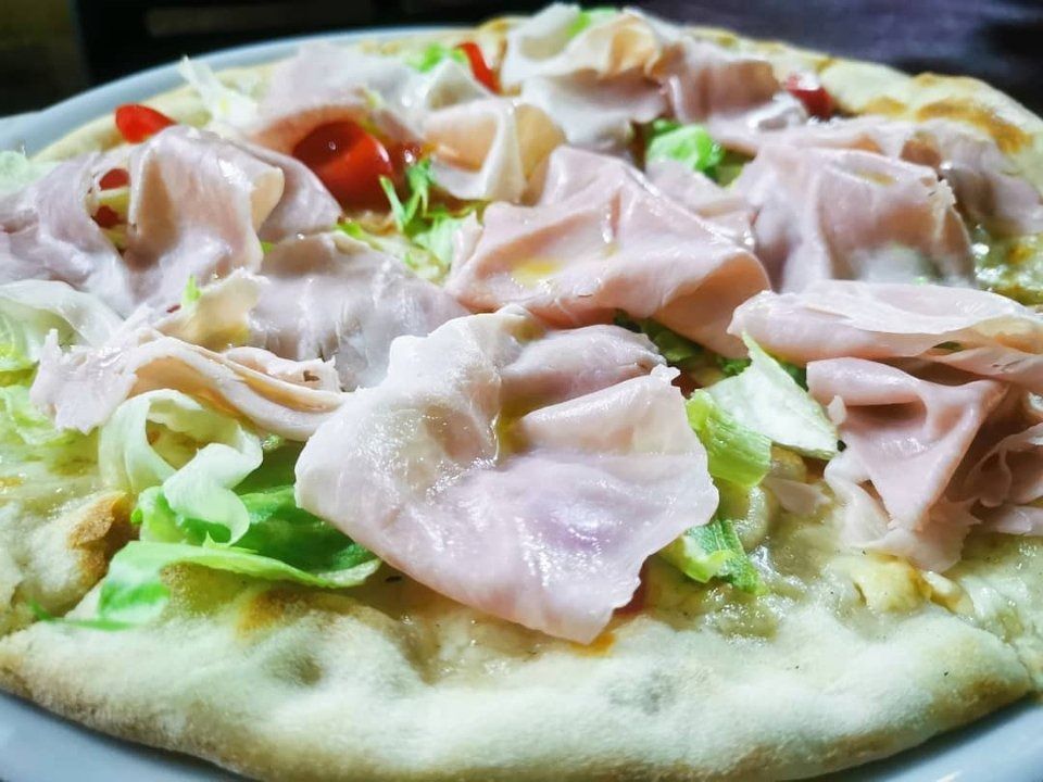 Primo piano di una pizza condita con prosciutto a fette, lattuga e pomodorini.