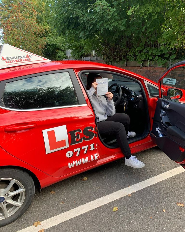 A person sits in the driver’s seat of a bright red driving school car, holding a document over their face.