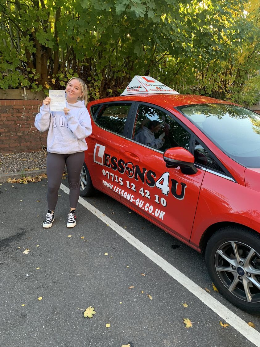 A person smiling while holding a document next to a bright red driving school car parked outdoors.