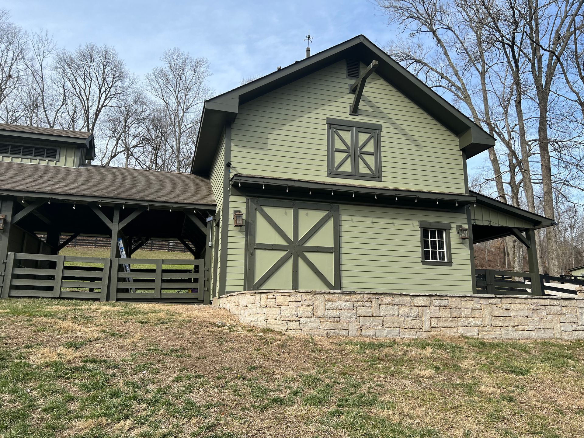 A green barn with a wooden fence in front of it.