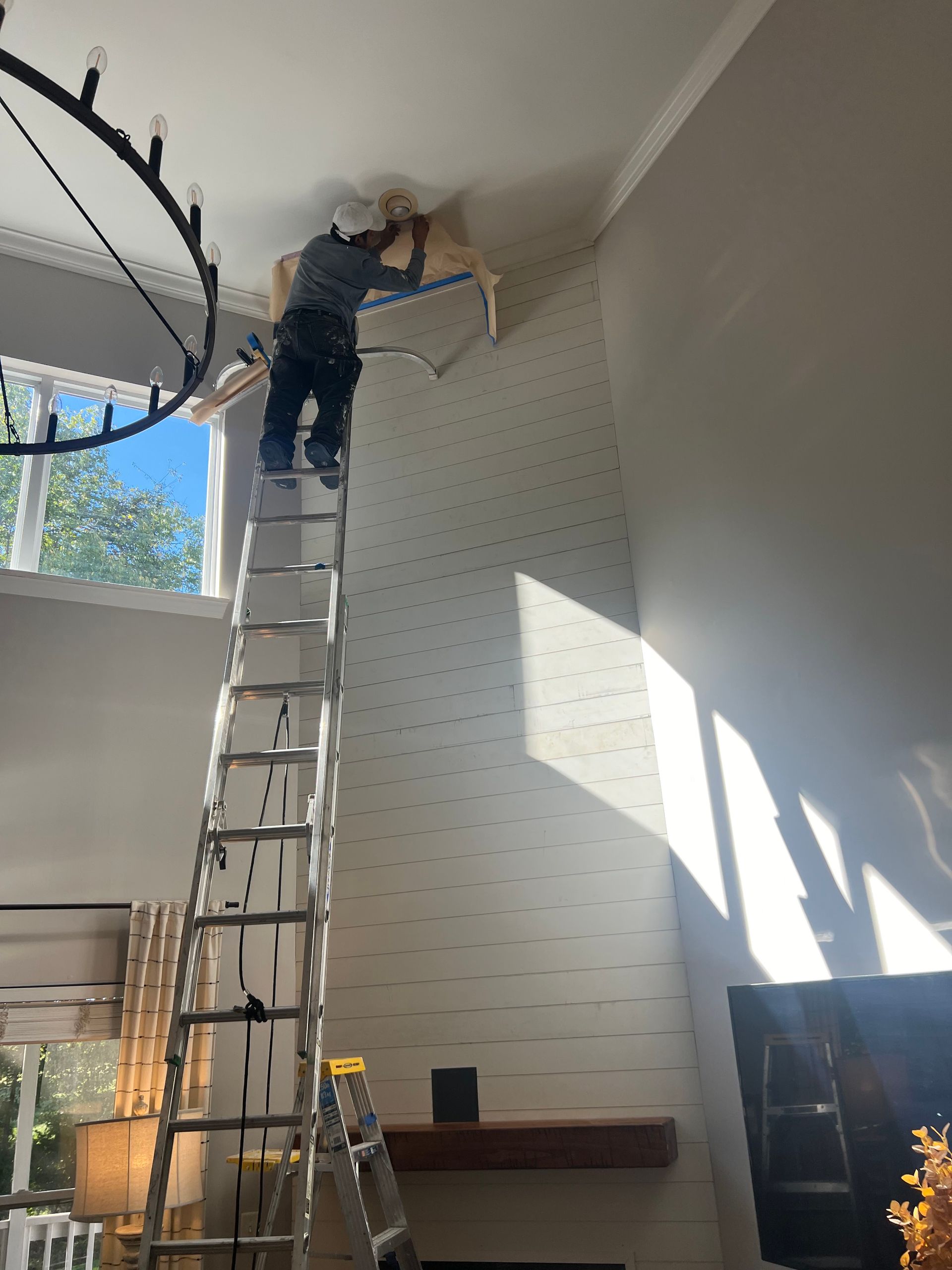 A man is standing on a ladder in a living room.