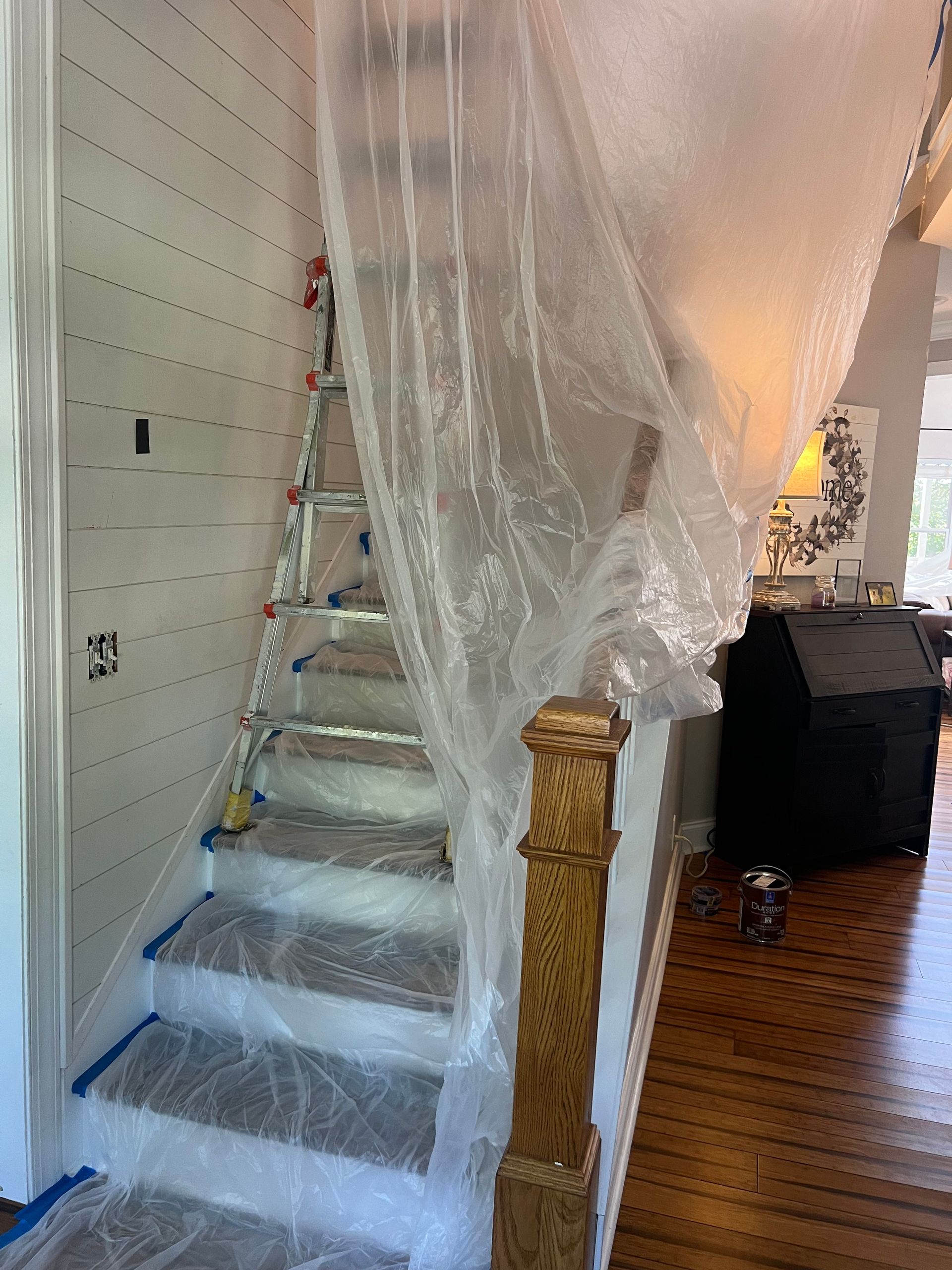 A ladder is sitting next to a staircase covered in plastic wrap.
