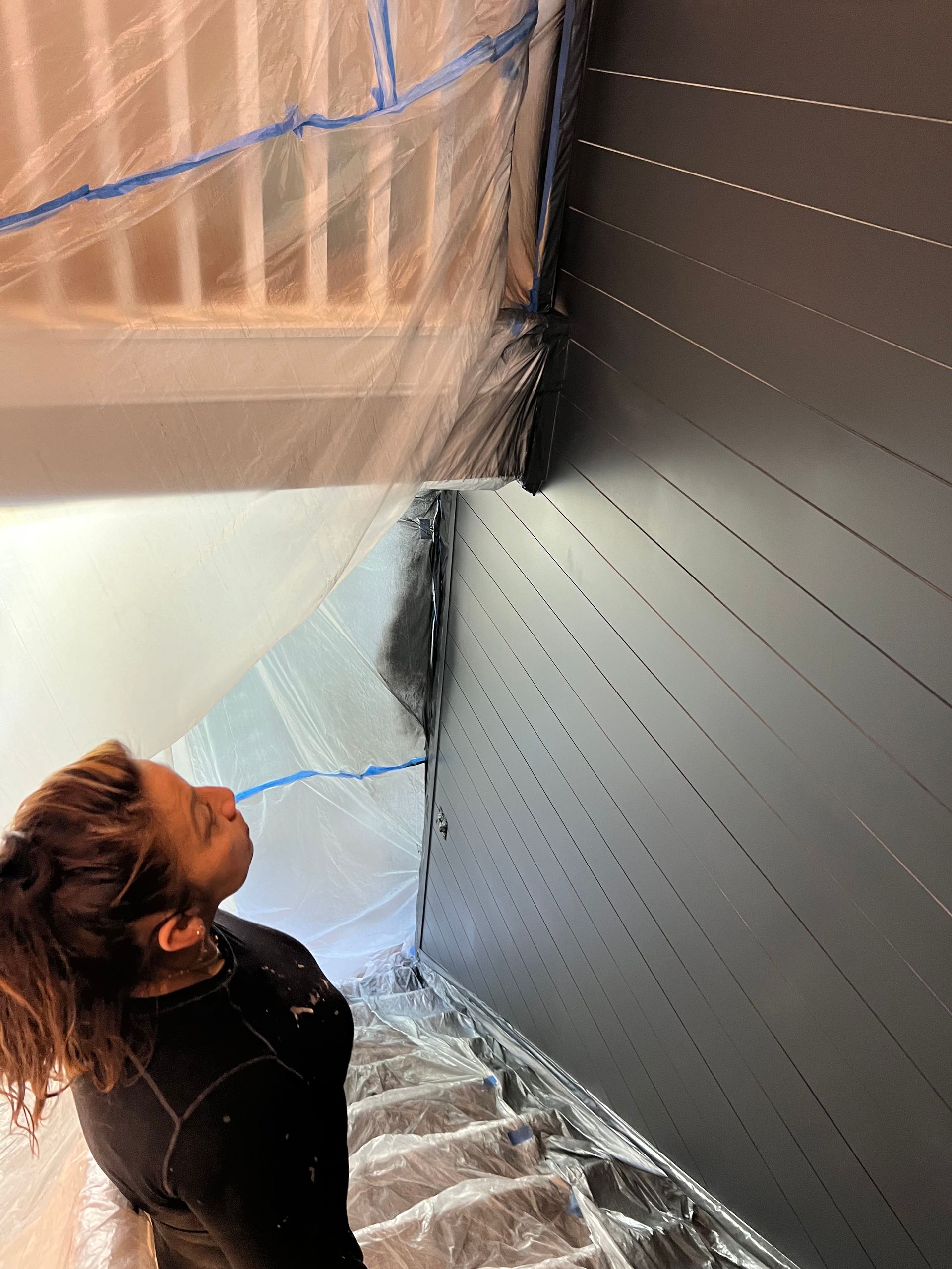 A woman is standing in front of a black wall covered in plastic.