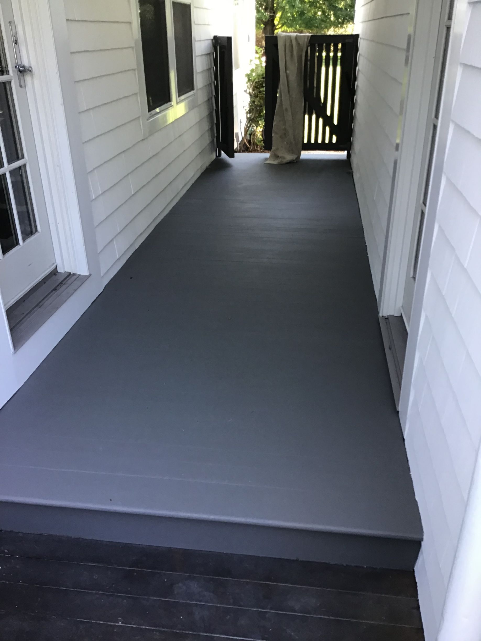 A gray porch with a white house in the background.