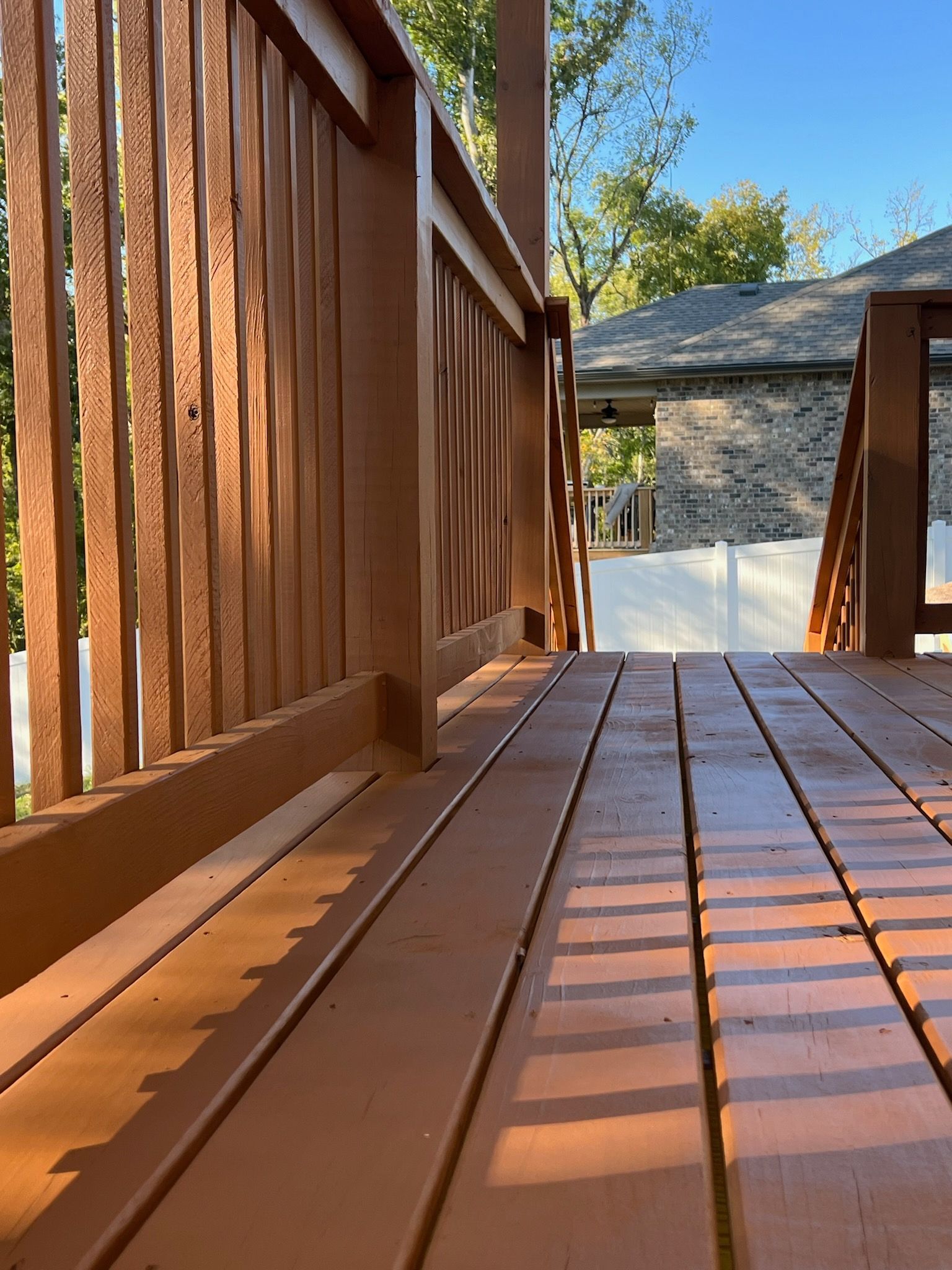 A wooden deck with a wooden railing and stairs leading to a house.