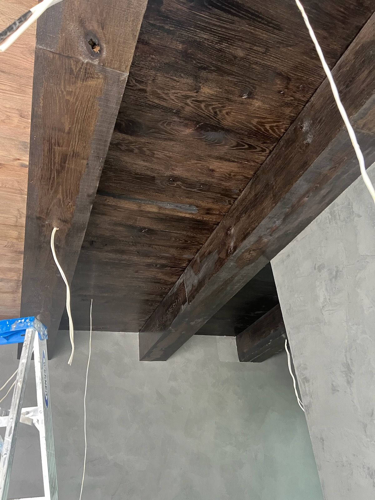 A ladder is sitting under a wooden ceiling in a room.