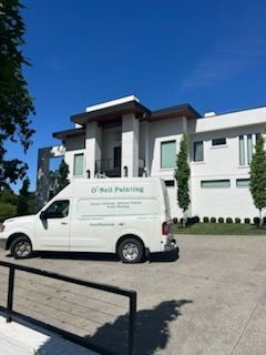 A white van is parked in front of a large white house.