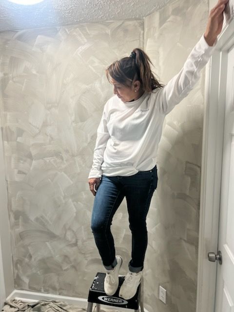 A woman is standing on a stool while painting a wall.