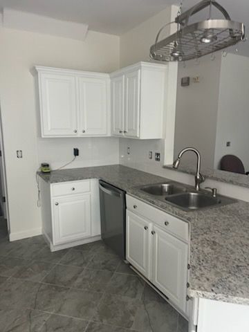 A kitchen with white cabinets , granite counter tops , a sink and a dishwasher.