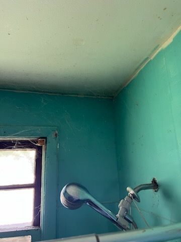 A shower head is hanging from the ceiling in a bathroom next to a window.