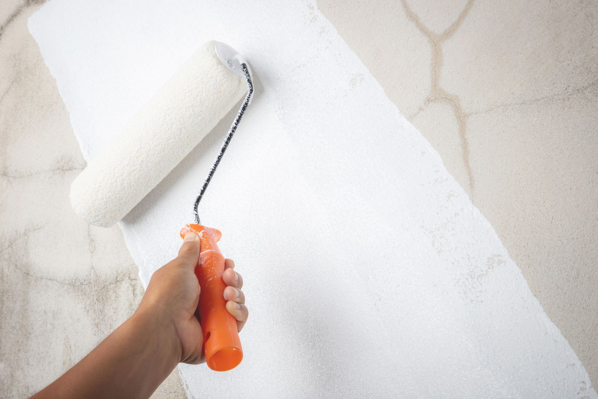A person is painting a wall with a paint roller.