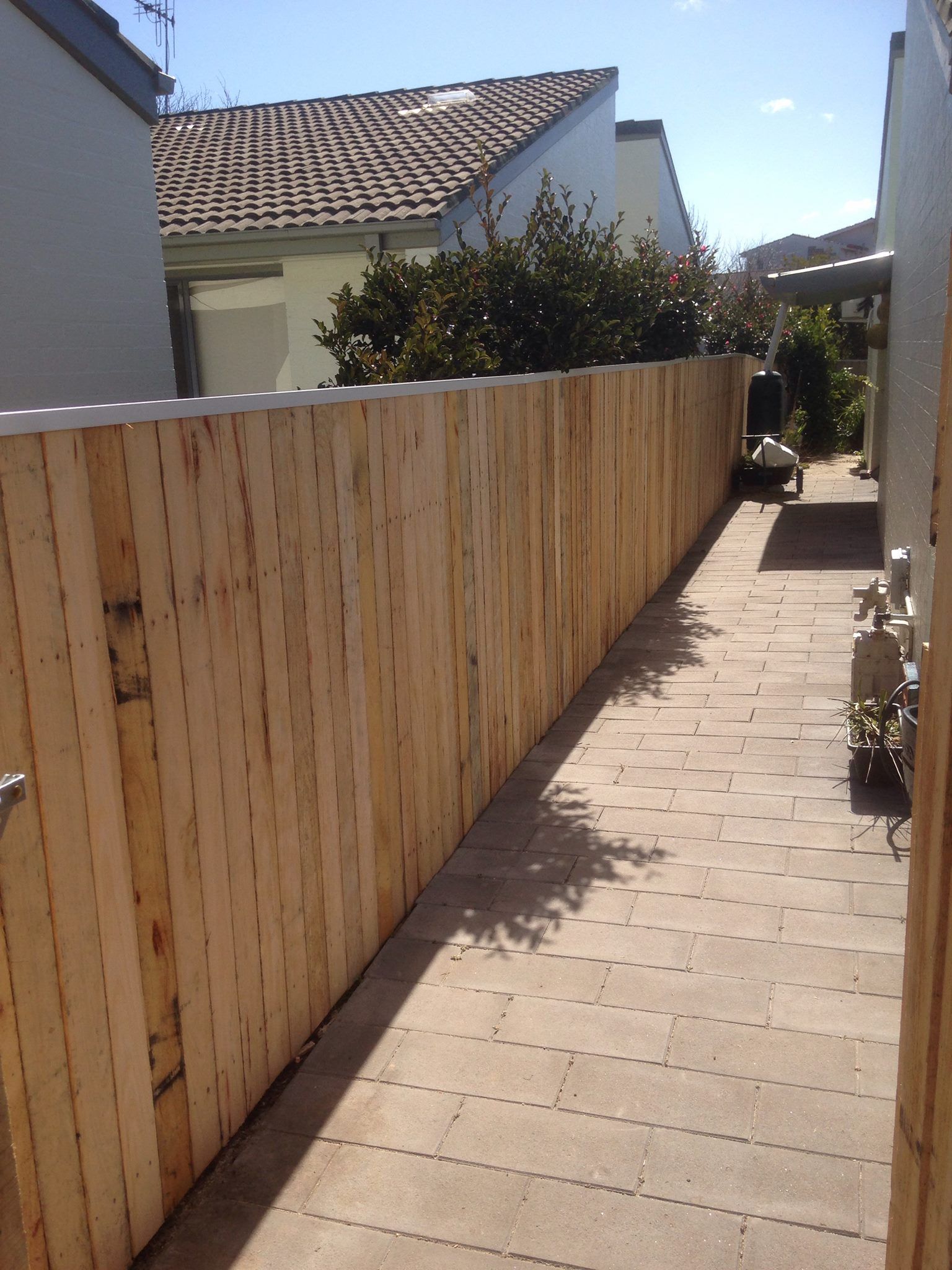 A long wooden fence along a sidewalk between two houses