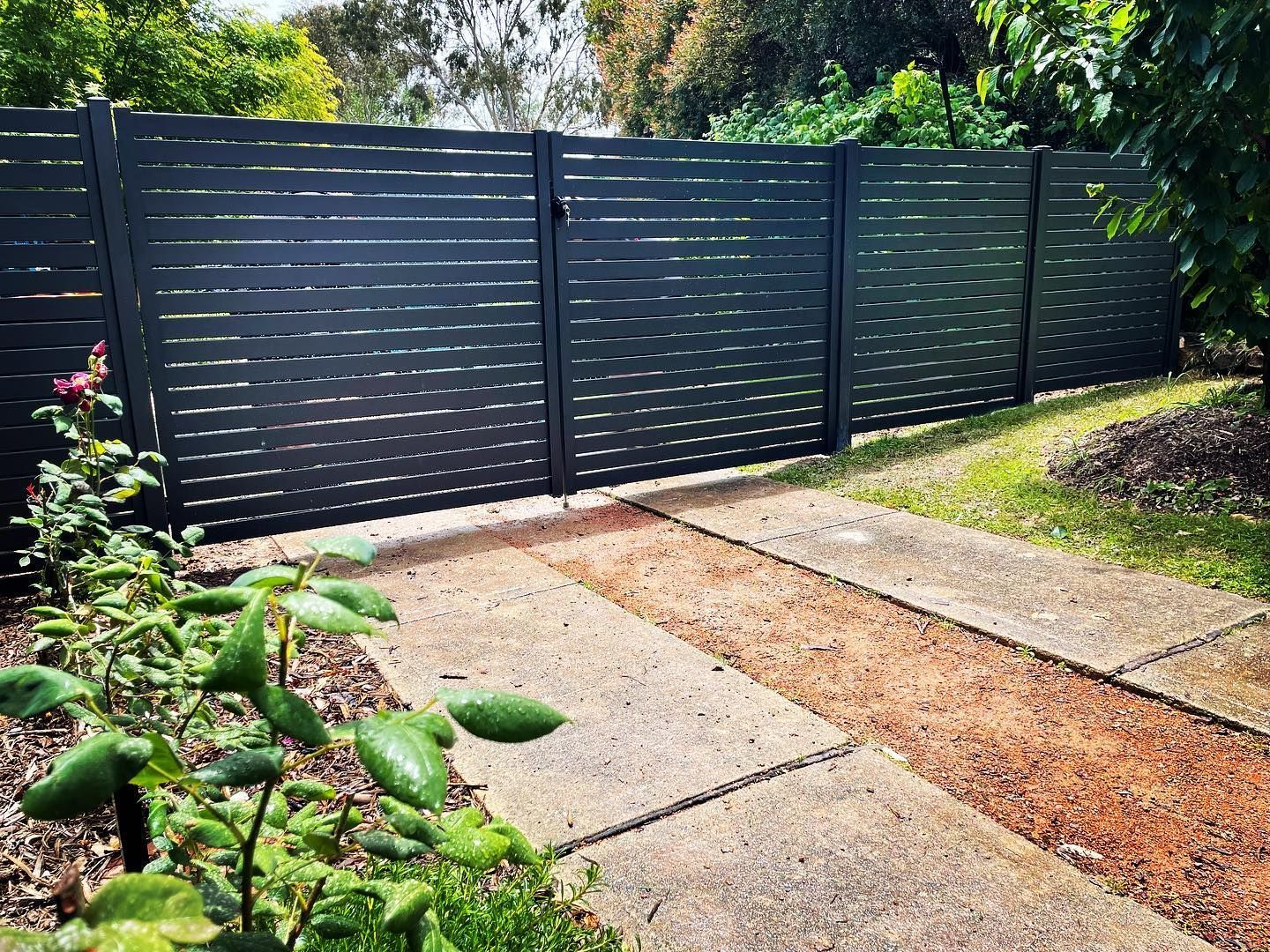 A black wooden fence and gate surround a concrete driveway.
