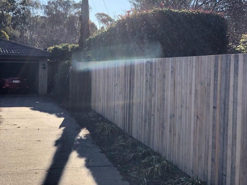A wooden fence is along the side of a road next to a garage.