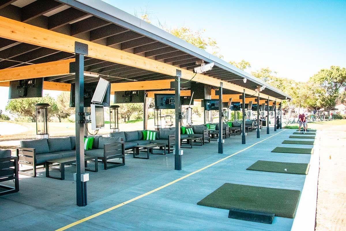 A row of lawn chairs and tables under a canopy at a golf course.