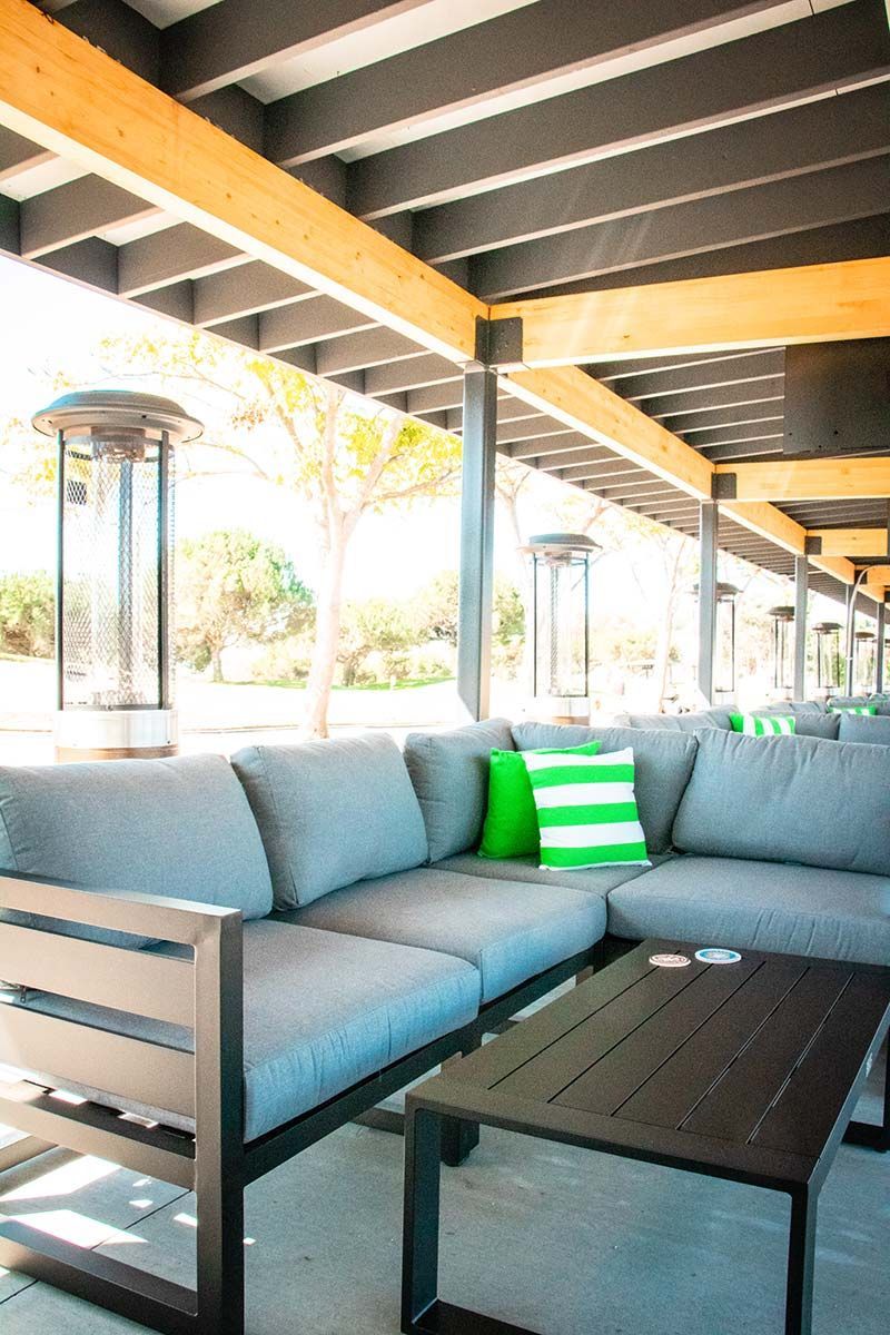 A patio area with a couch , table , and heaters.