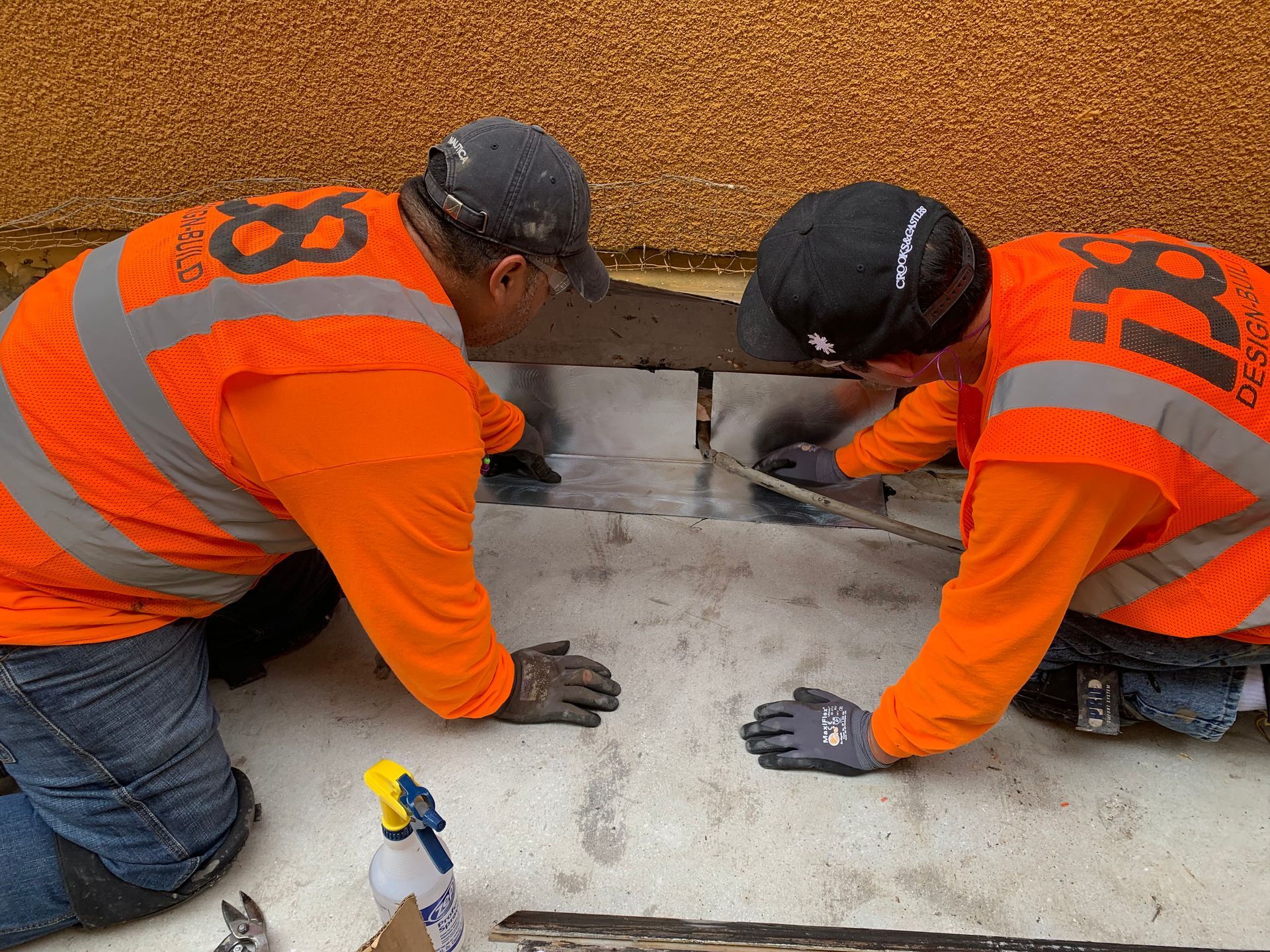 Two men in orange vests are kneeling down on the ground.