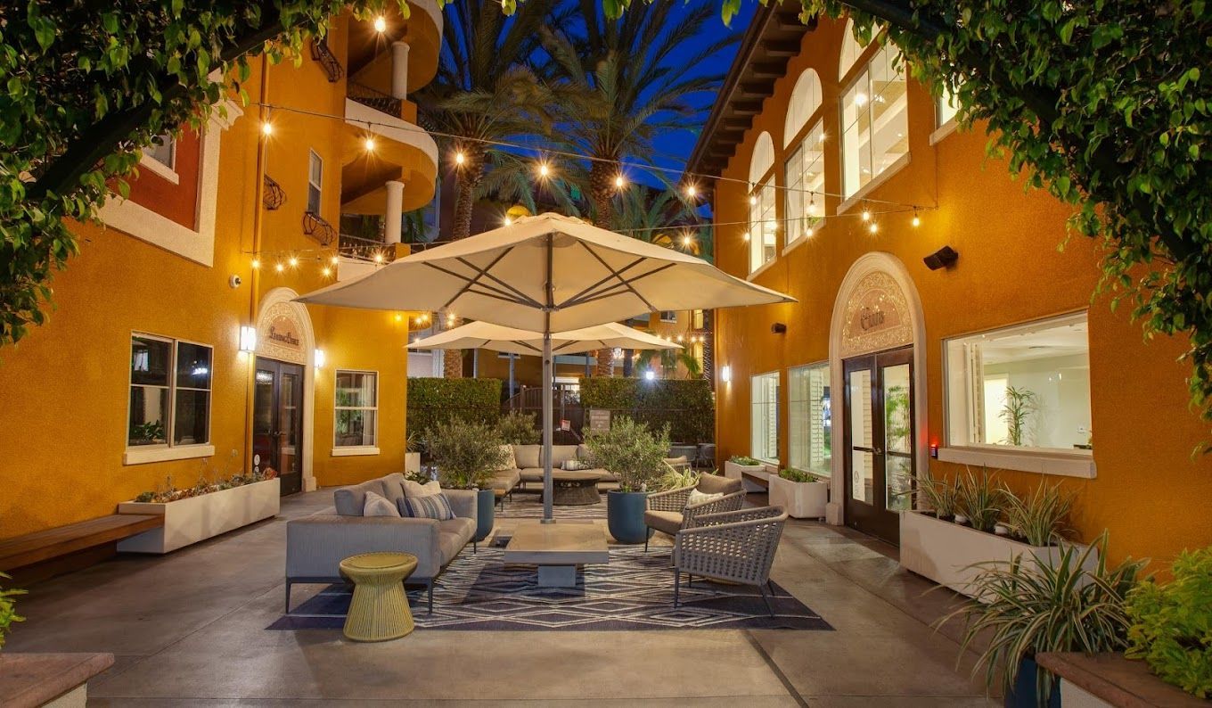 A courtyard with umbrellas and furniture in front of a building at night.