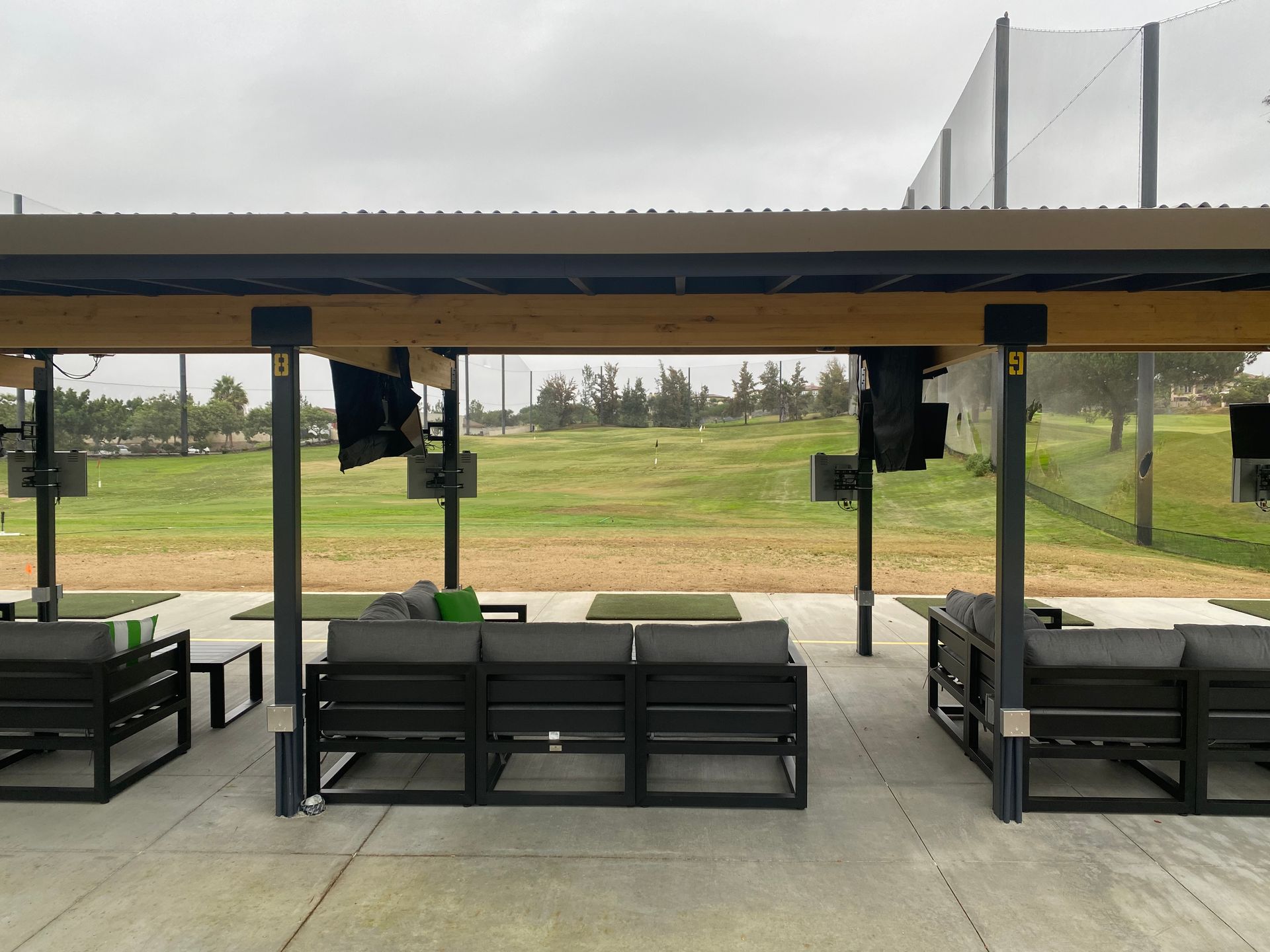 A covered area with a lot of furniture and a golf course in the background