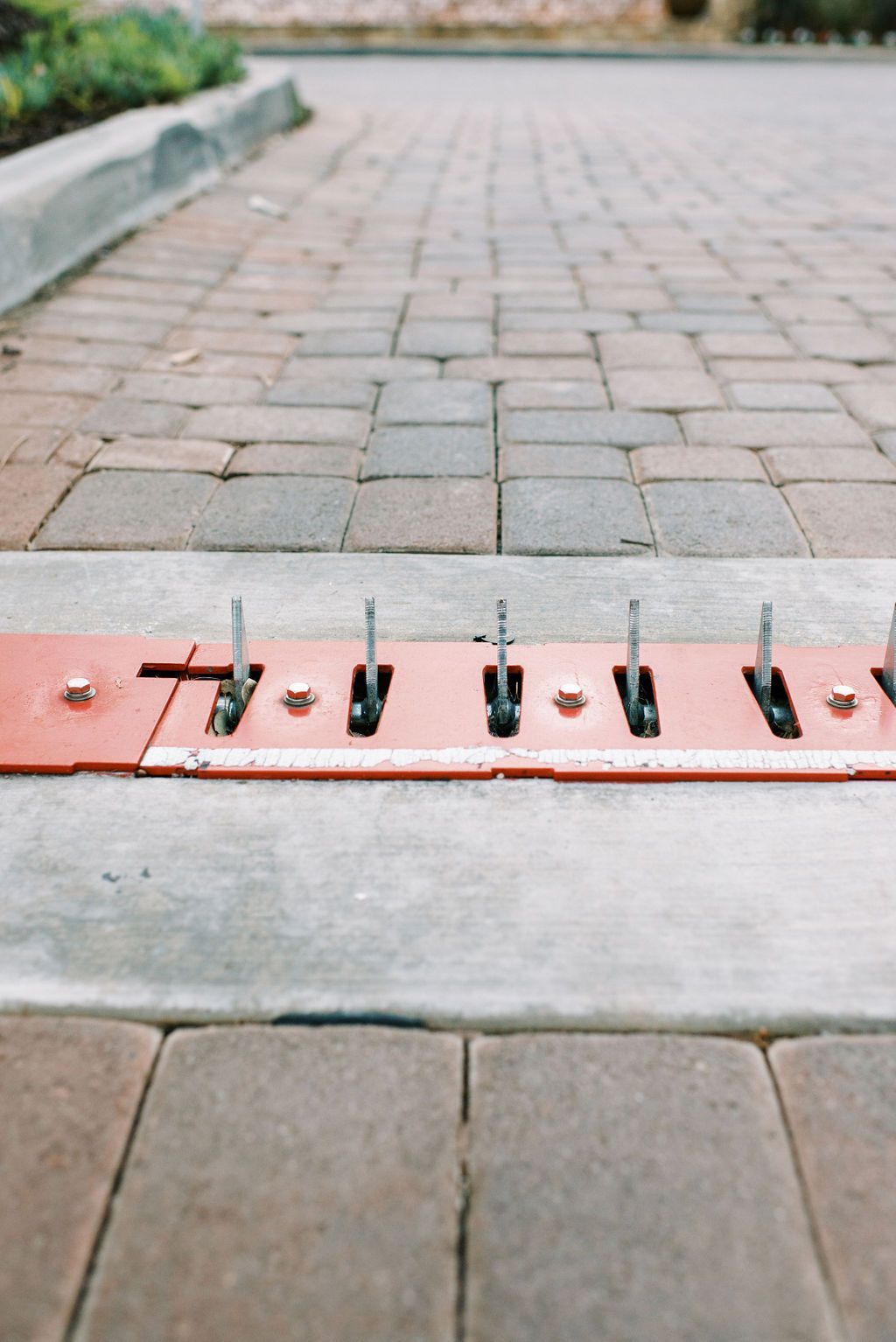 A red barrier is sitting on the side of a brick road.