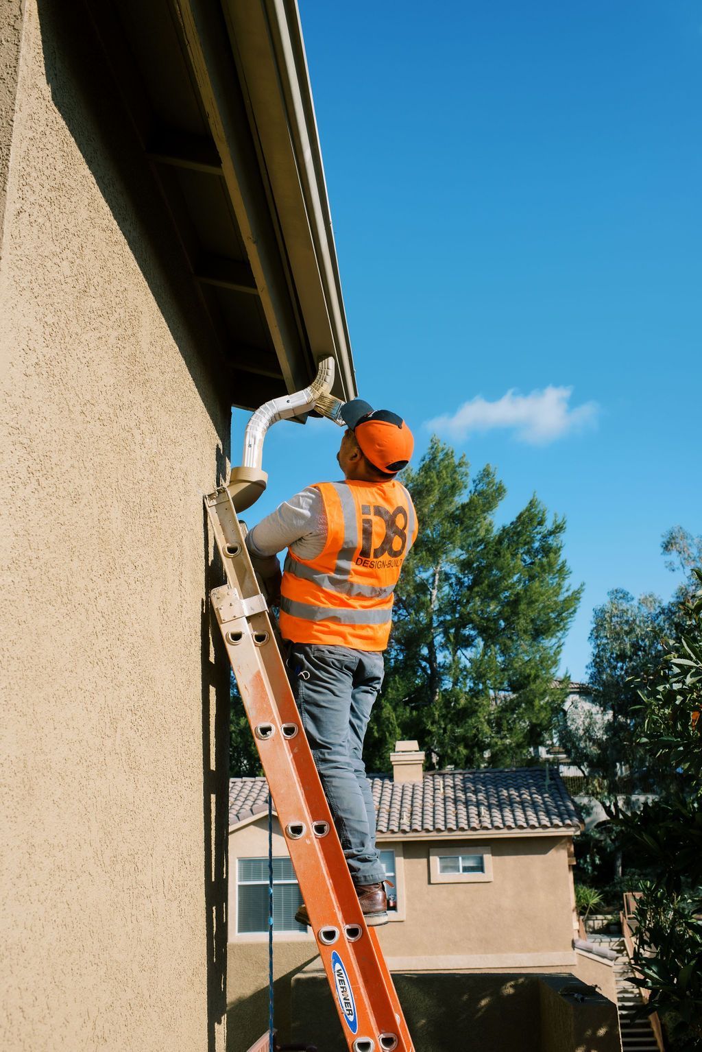 A man is standing on a ladder fixing a gutter on a house.