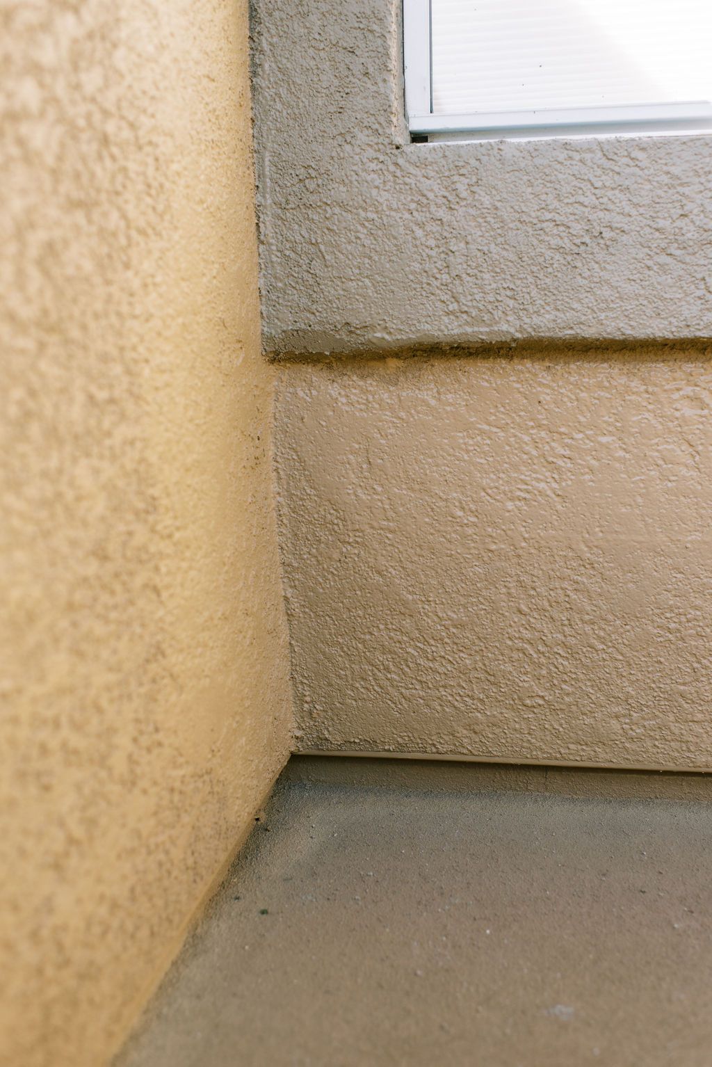 A corner of a building with a window and a concrete floor.
